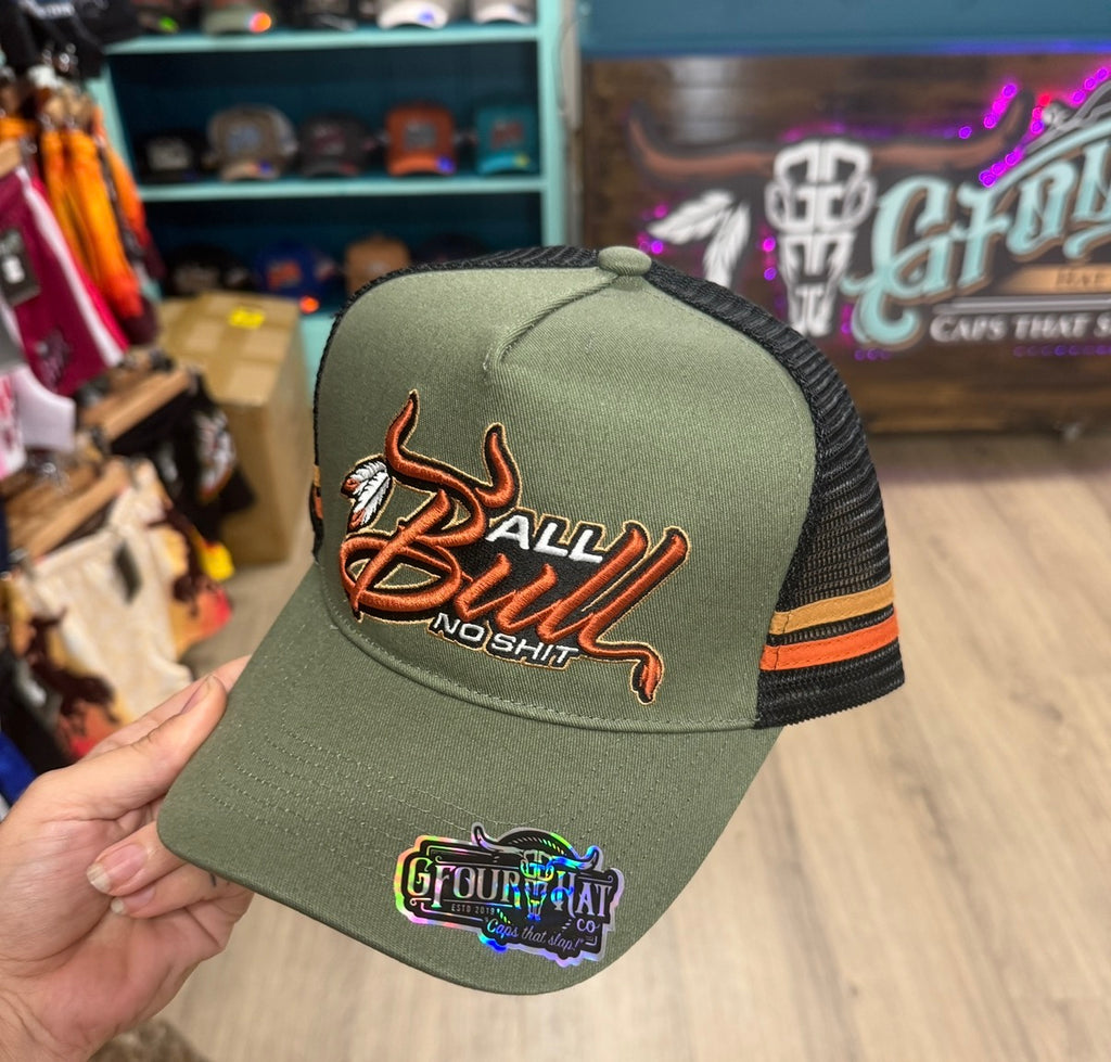 Green cap with 'All Bull No Shit' text held by a hand in a store setting.